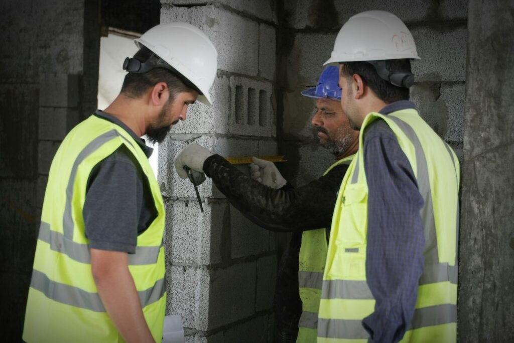 Engenheiros com capacete e colete inspecionando parede de blocos de concreto em obra
